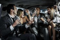 Two cheerful businessmen sitting with two young women in a limousine and having fun.